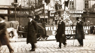 Cena de uma manifestação ou desfile ocorrido em 1º de maio de 1919 em Budapest, na rua Rákóczi, na antiga república soviética na Hungria. Na fotografia em preto e branco, pode-se observar signos políticos nas ruas