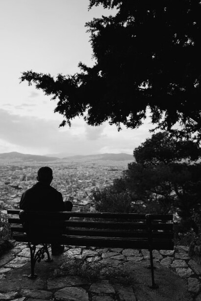 An elderly man sitting on a brown bench, gazing out at the sea