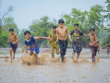 Um grupo de meninos corre pela rua sob a chuva, levantando água a cada passo. A brincadeira transforma o espaço cotidiano em território de aventura, como nas lembranças do autor sobre as ruas de sua infância