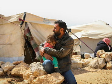 A man holds his daughter at a displacement campsite in Idlib, Idlib Governorate, Syria