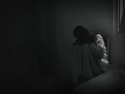 A person hiding in their room, with their body held close to them. The mental development of the human being is poor