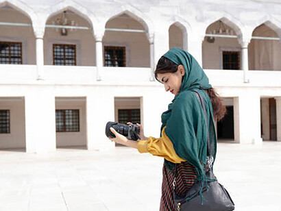 In the heart of the city, a young woman tourist, wearing a hijab that blends seamlessly with her stylish ensemble, passionately captures the urban landscape through the lens of her camera