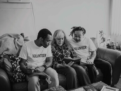 Two volunteers reading with an elderly man in his home