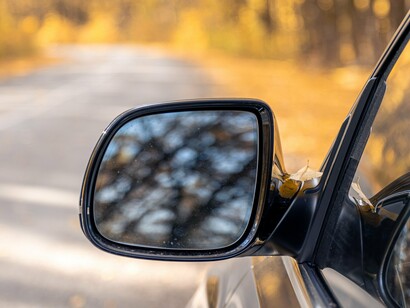 A rear view mirror capturing the road behind as the journey continues forward, representing reflection and a deeper understanding of the past