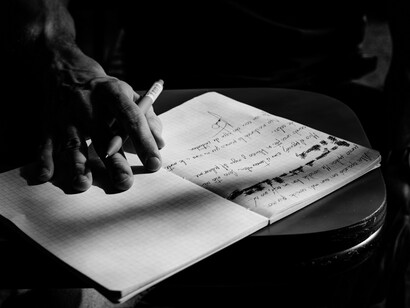 Una persona escribe a mano en un cuaderno cuadriculado mientras revisa anotaciones realizadas previamente