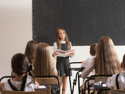 In the classroom, schoolchildren are focused on their lesson, with the blackboard in front of them
