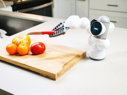 A small robot, with AI, cuts tomatoes on a cutting board in the kitchen