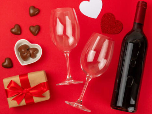 A cozy setting featuring a bottle of red wine, heart-shaped chocolates, and a thoughtful gift, all arranged on a vibrant backdrop