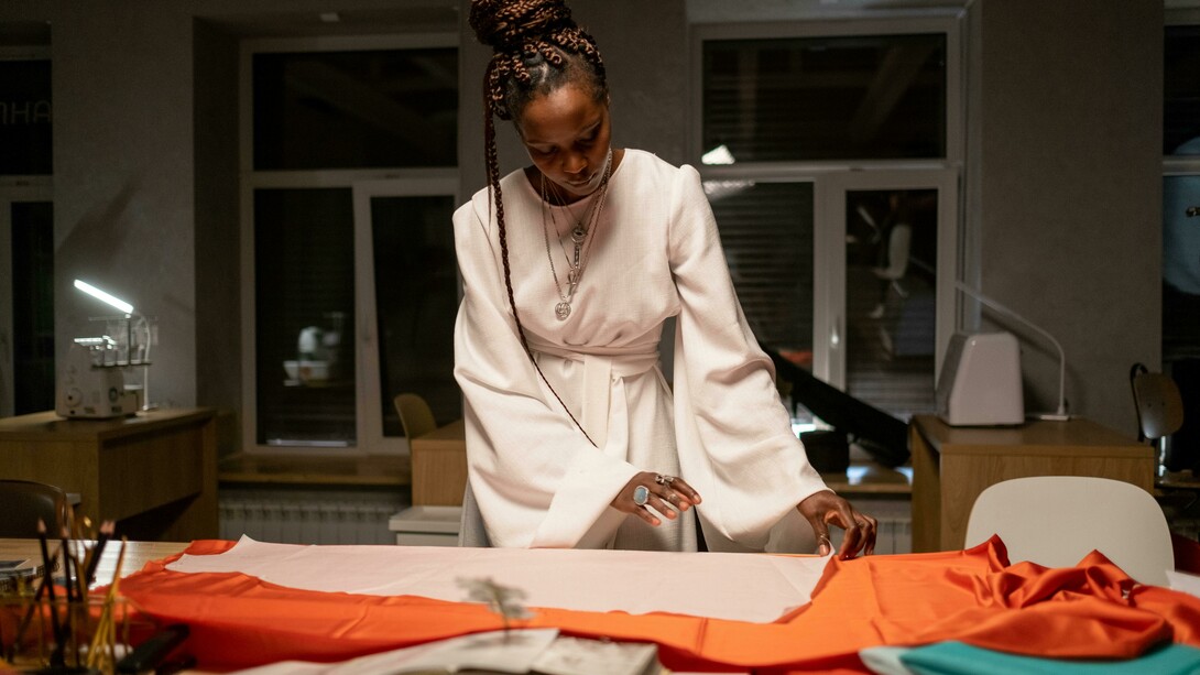 A fashion designer stands at her workspace, arranging and examining fabrics