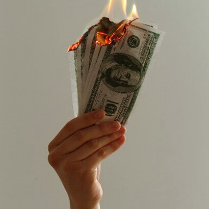 As a symbol of the economic crisis, a person holds lighted dollar bills, representing the rapid erosion of wealth and financial turmoil