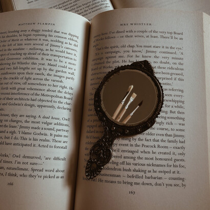 Livro, espelho e alguns pinceis retratam a importância da leitura e arte manual