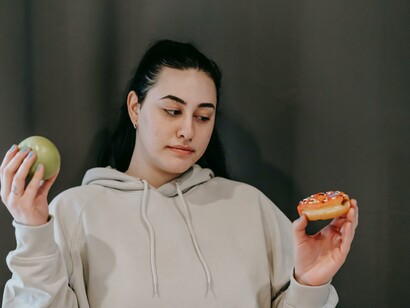 Mulher olha para a rosquinha enquanto segura uma maçã