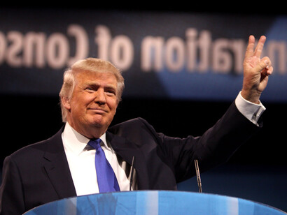 Donald Trump at a conference, holding his arm up and doing the V sing