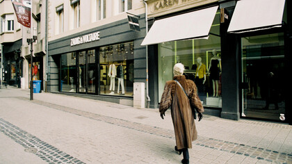 Stylish woman in a brown fur coat passing by the storefronts of high-end brands such as Zadig & Voltaire