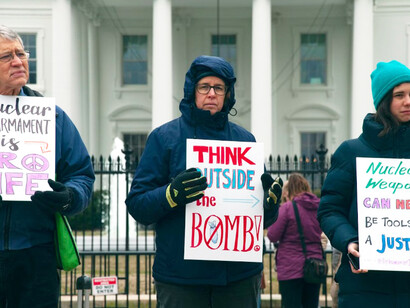 Two men and a woman hold protest signs in front of the White House in Washington, D.C., during a daytime anti-nuclear demonstration