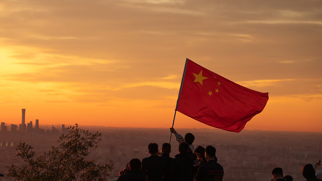 A group of people stands atop a hill, proudly holding the flag of China, with Beijing in the background