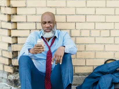 A drained man sitting quietly outside an urban building, symbolising the quiet despair many people feel in today’s economic climate