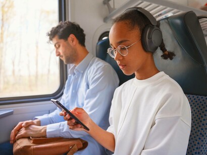Una ragazza ascolta musica con le cuffie e guarda il cellulare, mentre l’uomo accanto a lei riposa durante il viaggio in treno