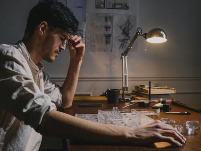An architecture student working at home, while others collaborate on models in a hands-on learning environment