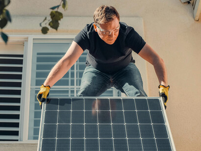 A man stands on a rooftop installing a solar panel