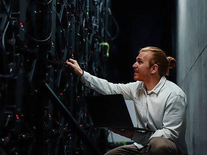 Technician holding a laptop while observing an LED wall display in a server room environment