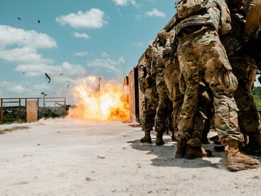 Militares observam uma explosão controlada durante um exercício de treinamento, mantendo-se próximos ao local da detonação. A imagem revela a preparação sistemática para situações de conflito e o domínio técnico necessário para lidar com a força destrutiva dos explosivo