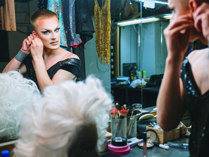 As the mirror reflects a kaleidoscope of colours, the drag queen meticulously applies makeup, transforming into a vibrant persona ready to captivate the audience