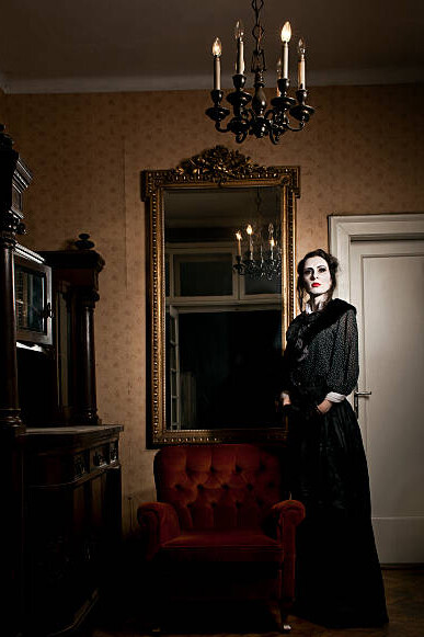 A ghostly woman stands beside an armchair, reflected in a Victorian-era mirror