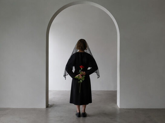 A woman in a black dress holds a red rose, symbolizing grief, loss, and remembrance
