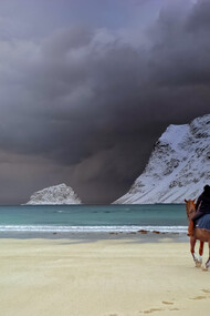 A woman rides a horse near the beach as a storm comes in