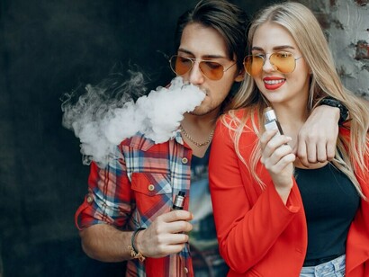 Young couple vaping in an urban cityscape, exhaling vapor as they pose confidently