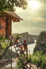A couple sits on a brown wooden ladder in Bali, Indonesia, enjoying a quiet moment