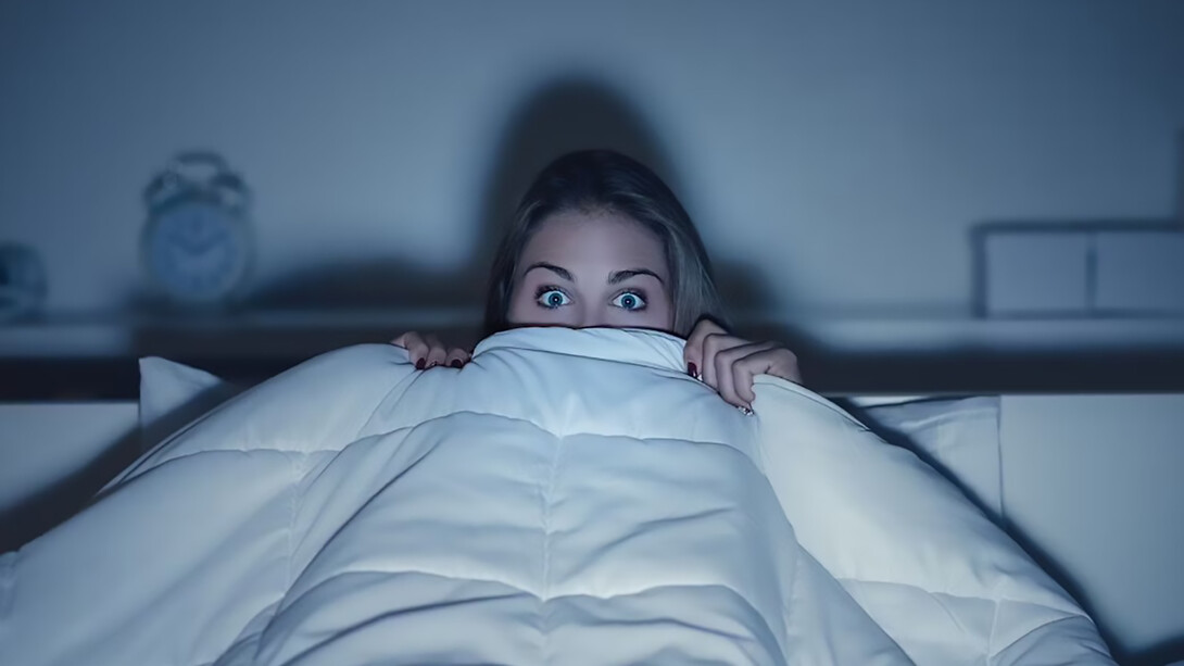 A woman, wrapped in a blanket, enjoying a horror movie with a frightened expression