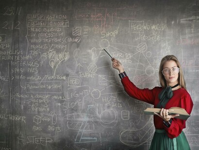 An educator pointing to the blackboard as her role might be replaced with an AI
