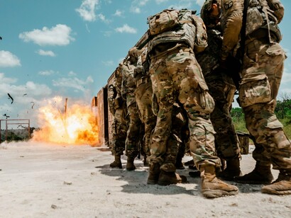 Soldiers taking cover during an explosion, representing the persistence of modern warfare in a volatile world