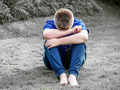 Boy with arms wrapped around knees in sadness and shame