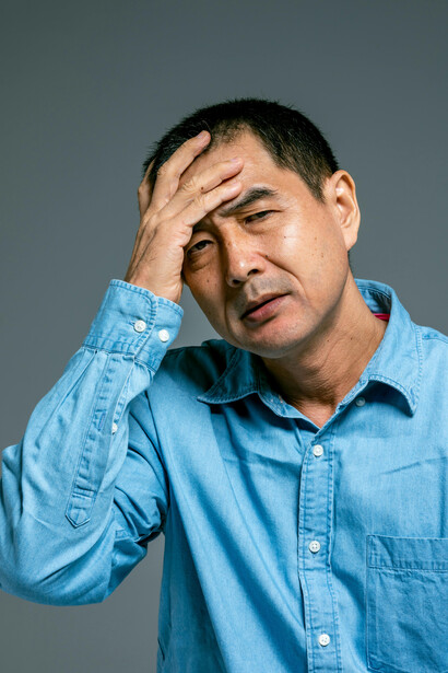 A man in a blue denim shirt stands anxiously, visibly burdened by fear and unease
