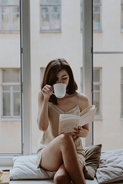 Bathed in soft morning light, a woman reads by the window, her thoughtful expression suggesting a moment of gentle melancholy