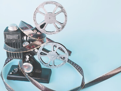 Captured against a blue backdrop, an aerial view features film strips, a film reel, and assorted camcorders, illustrating the multifaceted world of cinematography and filmmaking