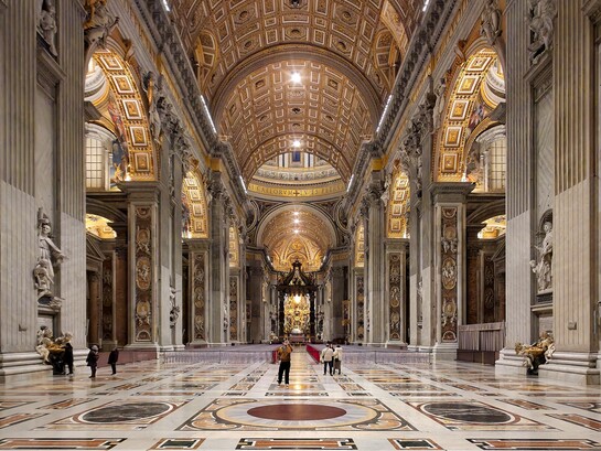 La navata centrale della Basilica di San Pietro si apre come un immenso spazio solenne e luminoso, scandito da colossali pilastri e ornato da marmi policromi e mosaici dorati, che guidano lo sguardo verso l’altare papale. Foto di Nate Bergin. Basilica di San Pietro, Città del Vaticano