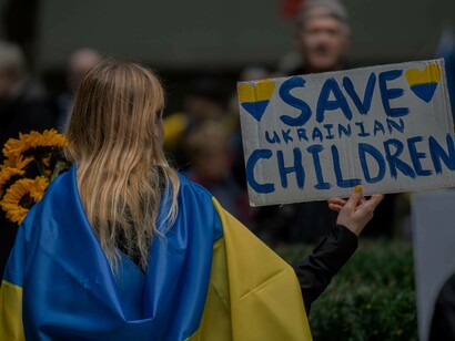 A girl holding a Save the Ukrainian Children, wrapped in the Ukraine flag during an anti-war protest