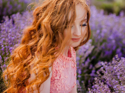 A young woman with flowing red hair amidst a sea of lavender blossoms