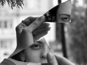 Uma jovem observa o próprio reflexo dividido entre os fragmentos de um espelho quebrado. Quando as certezas que sustentam nossa visão de mundo são colocadas em dúvida, aquilo que parecia inteiro pode revelar-se apenas uma construção