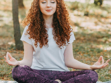 Woman practicing yoga on the grass in a park, looking healthy and relaxed