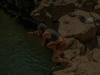 A girl gets ready to jump into the cold river from the edge of the rocks above