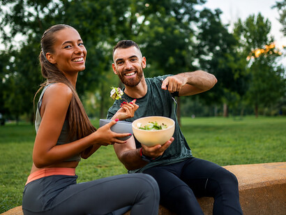 Fit and cheerful couple sharing a fresh vegetable salad after completing an intense workout outdoors
