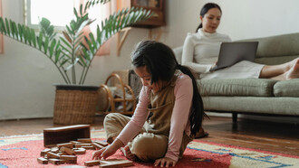 Niña con juguetes y mujer recostada en un sillón con una computadora