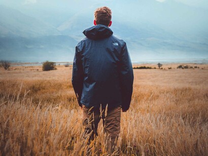 A man in a field on a winter's day is looking over the horizon and seeing the gigantic obstacle that is a mountain and questions whether he can overcome it