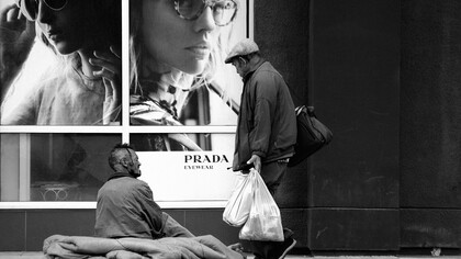 Homeless man in front of a high-end shop: inequality is a byproduct of profit maximization