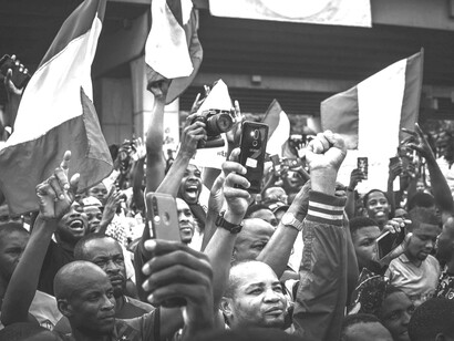 Black-and-white image of protesters in a crowd, raising smartphones, Nigeria